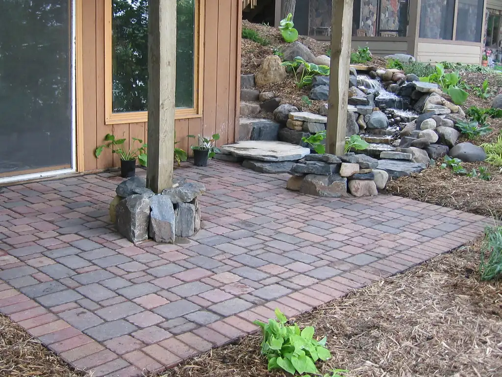 Brick paver patio beside a backyard waterfall and planting beds