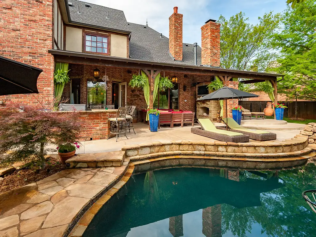 Natural stone pool deck and patio behind a brick home